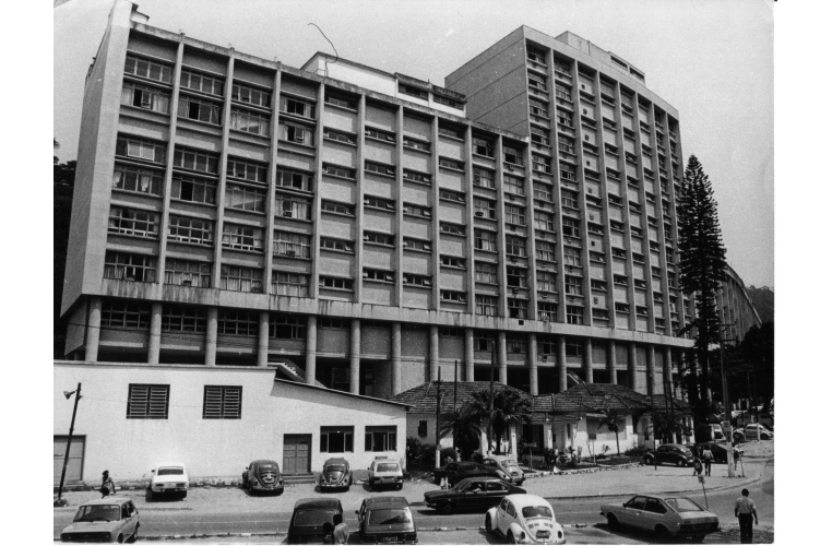 Fachada do Edifício Cardeal Leme vista a partir da entrada da Ala Frings. Vemos os carros estacionados e as casas da Vila. c. 1980. Fotógrafo Antônio Albuquerque. Acervo do Projeto Comunicar.